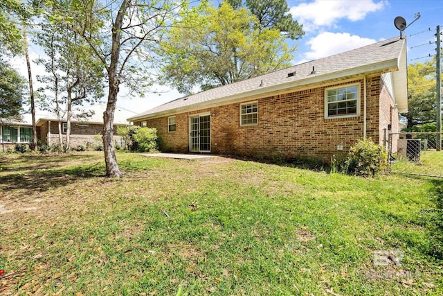 rear view of house with a lawn, brick siding, and fence