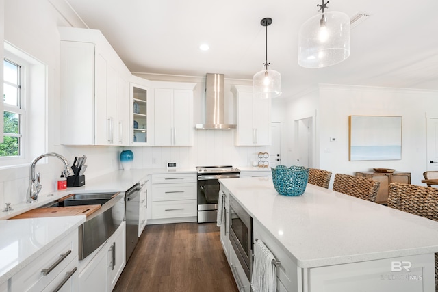 kitchen featuring pendant lighting, white cabinets, appliances with stainless steel finishes, dark wood-type flooring, and wall chimney exhaust hood