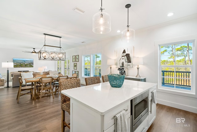 kitchen featuring stainless steel microwave, a kitchen island, decorative light fixtures, white cabinetry, and hardwood / wood-style flooring