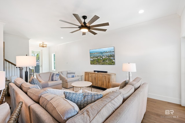 living room with crown molding, ceiling fan with notable chandelier, and light wood-type flooring