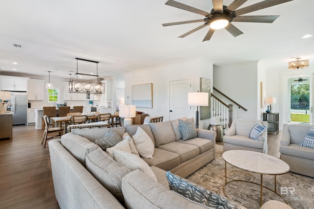 living room with a healthy amount of sunlight, ornamental molding, dark wood-type flooring, and ceiling fan with notable chandelier