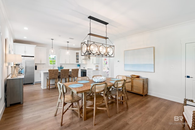 dining area featuring ornamental molding, sink, a chandelier, and light hardwood / wood-style flooring