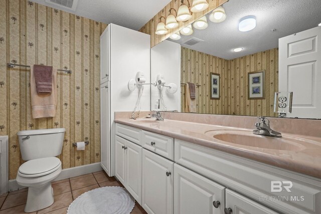 bathroom with tile patterned flooring, a textured ceiling, vanity, and toilet