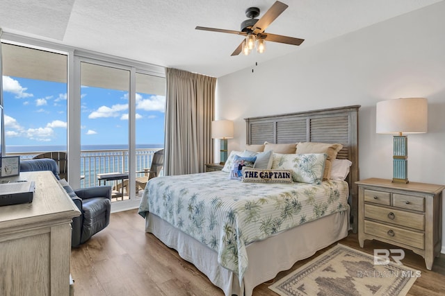 bedroom featuring a wall of windows, access to outside, a water view, and wood finished floors