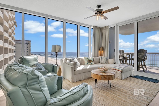 living room with a water view, a textured ceiling, a wall of windows, and a ceiling fan