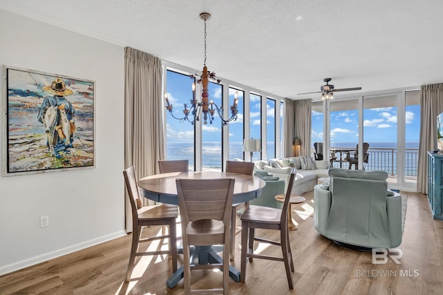 dining space with baseboards, wood finished floors, a wall of windows, a textured ceiling, and ceiling fan with notable chandelier