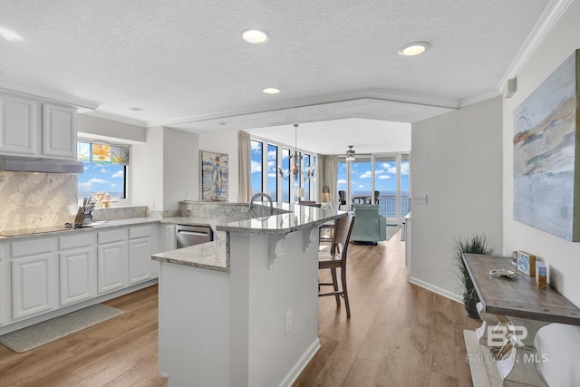 kitchen with black electric stovetop, a breakfast bar area, a peninsula, light wood-style floors, and dishwasher