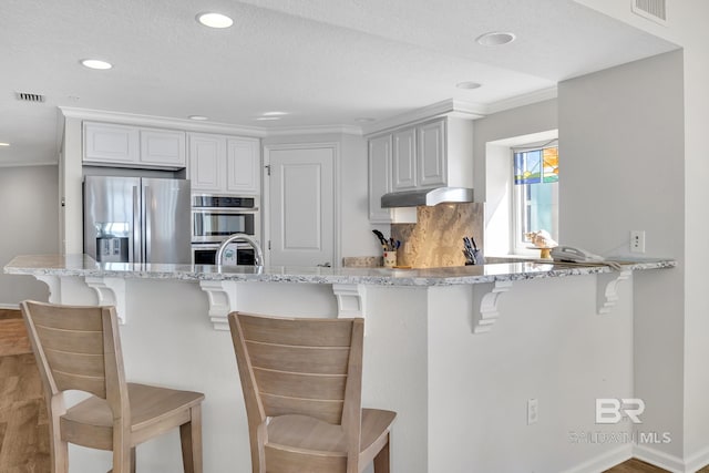 kitchen with a peninsula, appliances with stainless steel finishes, visible vents, and a kitchen breakfast bar