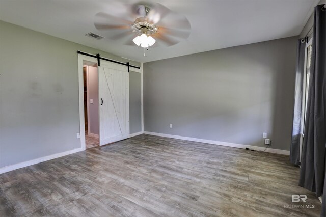 unfurnished bedroom featuring ceiling fan, a barn door, and hardwood / wood-style flooring