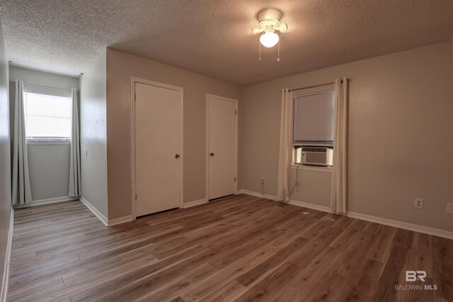 unfurnished bedroom featuring wood-type flooring, a textured ceiling, and cooling unit