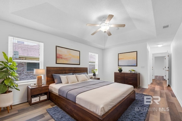 6950 Summerset Dr, Gulf Shores, AL 36542 - bedroom featuring a tray ceiling, wood finished floors, baseboards, and a ceiling fan