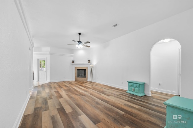 6950 Summerset Dr, Gulf Shores, AL 36542 - unfurnished living room featuring wood finished floors, ceiling fan, baseboards, a glass covered fireplace, and arched walkways