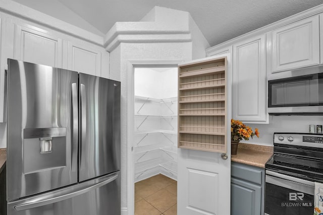 6950 Summerset Dr, Gulf Shores, AL 36542 - kitchen with stainless steel appliances, light tile patterned flooring, white cabinetry, and lofted ceiling