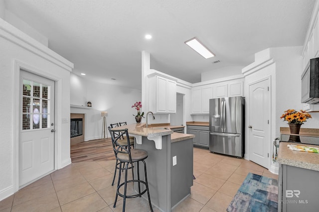 6950 Summerset Dr, Gulf Shores, AL 36542 - kitchen featuring stainless steel refrigerator with ice dispenser, a peninsula, light tile patterned floors, a kitchen breakfast bar, and a glass covered fireplace