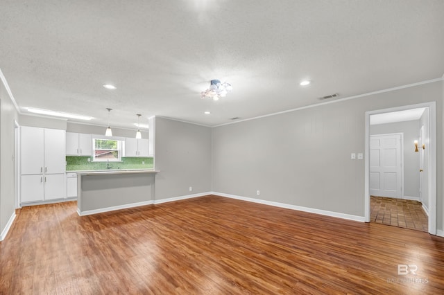 unfurnished living room with wood finished floors, crown molding, visible vents, and recessed lighting