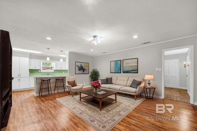 living area featuring recessed lighting, visible vents, light wood-style flooring, baseboards, and ornamental molding