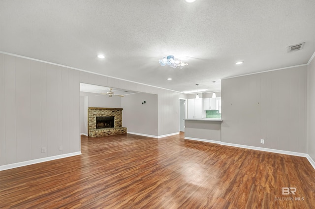 unfurnished living room with dark wood finished floors, a brick fireplace, visible vents, a ceiling fan, and a textured ceiling