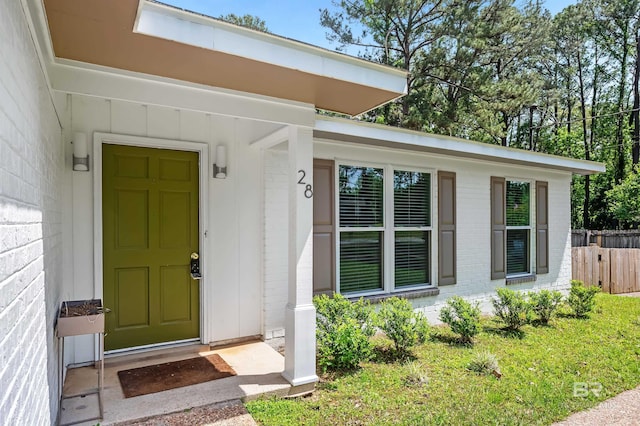 view of exterior entry featuring brick siding and fence