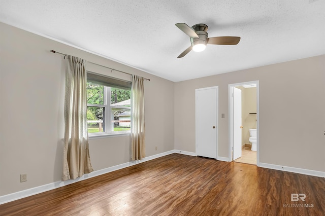 unfurnished bedroom featuring ensuite bathroom, a textured ceiling, wood finished floors, and baseboards
