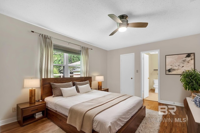 bedroom featuring a textured ceiling, connected bathroom, light wood finished floors, and baseboards