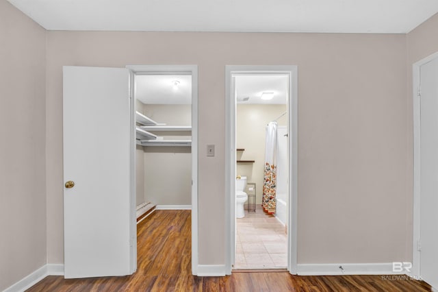 unfurnished bedroom featuring a closet, a walk in closet, baseboards, baseboard heating, and wood finished floors