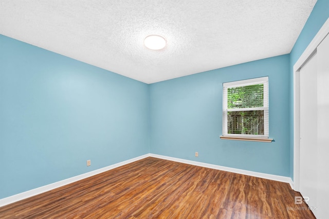 unfurnished room with a textured ceiling, wood finished floors, and baseboards