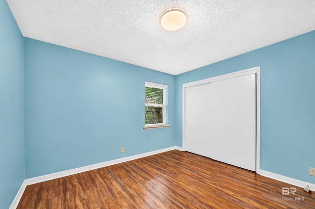 unfurnished bedroom with a closet, a textured ceiling, wood finished floors, and baseboards