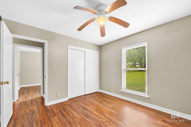 unfurnished bedroom with a textured ceiling, ceiling fan, a closet, baseboards, and wood finished floors