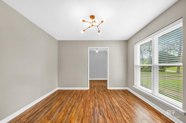 empty room featuring plenty of natural light, a notable chandelier, wood finished floors, and baseboards