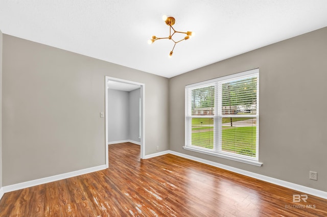 unfurnished room featuring baseboards, wood finished floors, and a notable chandelier