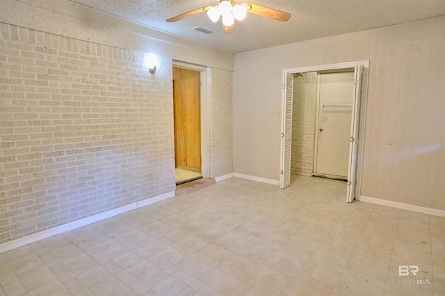 spare room featuring a textured ceiling, wood walls, ceiling fan, and brick wall