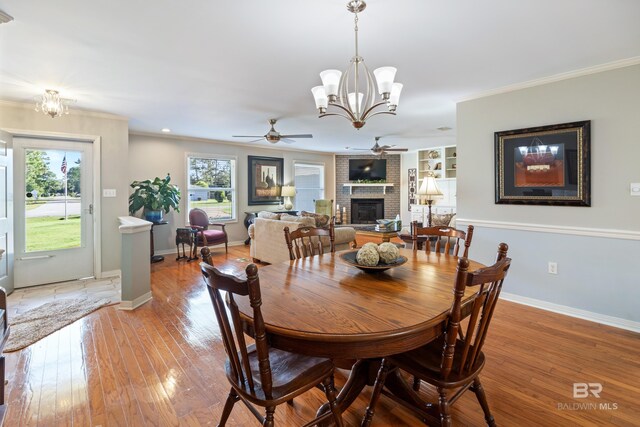 dining area featuring ceiling fan with notable chandelier, light wood-type flooring, crown molding, and a fireplace