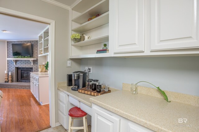 bar featuring white cabinets, light hardwood / wood-style flooring, a brick fireplace, and crown molding