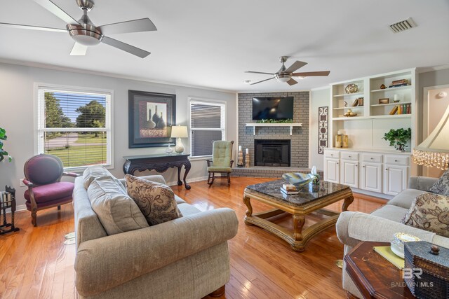 living room featuring a fireplace, crown molding, ceiling fan, and light wood-type flooring