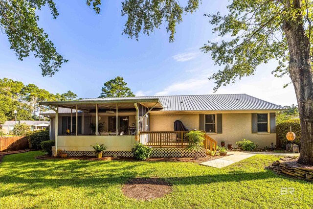 back of property featuring a wooden deck, a sunroom, and a lawn