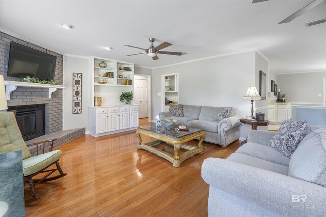 living room with a fireplace, ornamental molding, ceiling fan, and light wood-type flooring