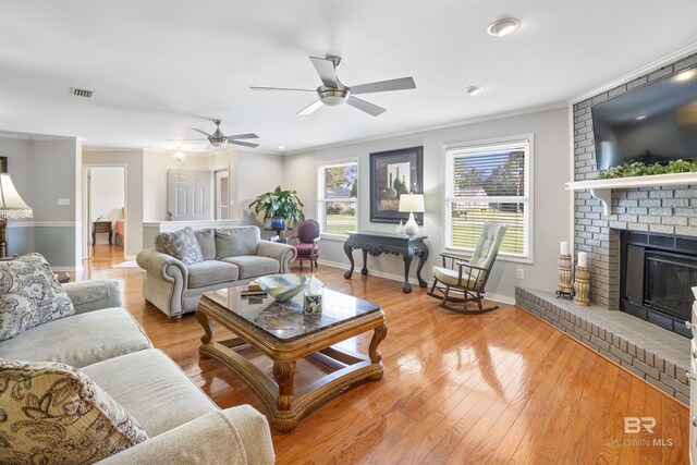 living room featuring light wood-type flooring, ceiling fan, a brick fireplace, and ornamental molding