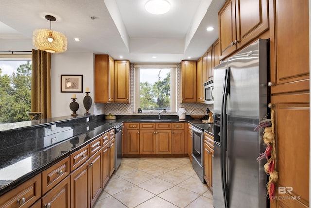 kitchen featuring brown cabinetry, a tray ceiling, stainless steel appliances, and decorative backsplash