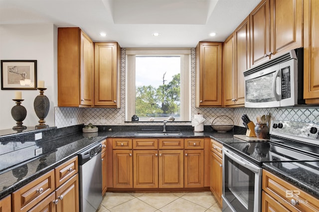 kitchen featuring appliances with stainless steel finishes, dark stone counters, light tile patterned flooring, and a sink