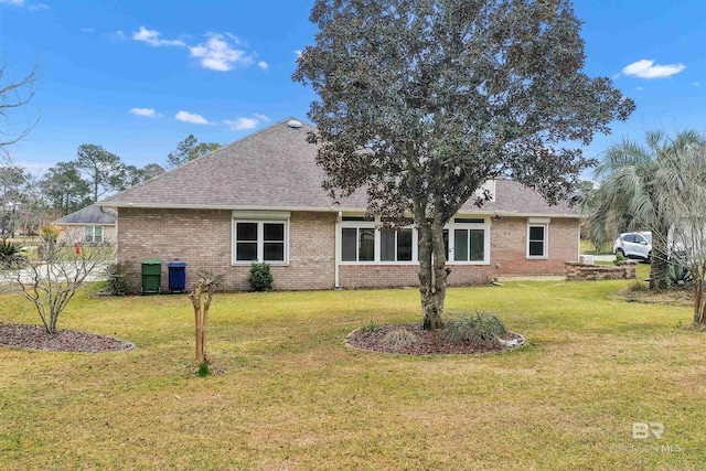 back of house with brick siding, roof with shingles, and a yard