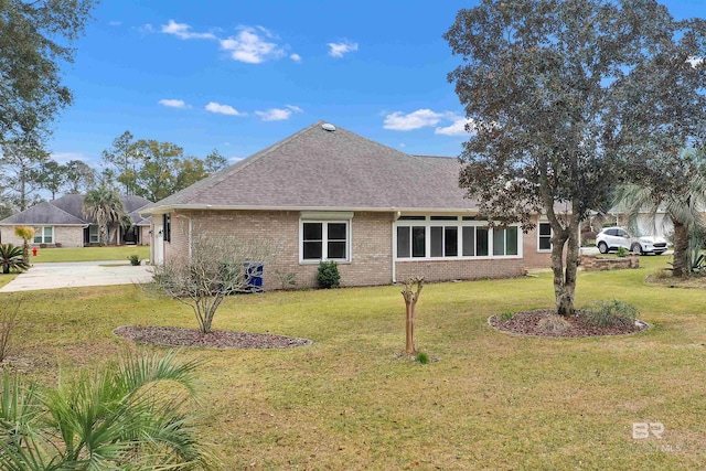 back of house with a yard, a shingled roof, concrete driveway, and brick siding