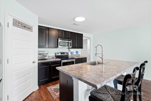 17372 Tallasee Blvd, Foley, AL 36535 - kitchen with stainless steel appliances, a breakfast bar area, a center island with sink, and dark wood-style flooring