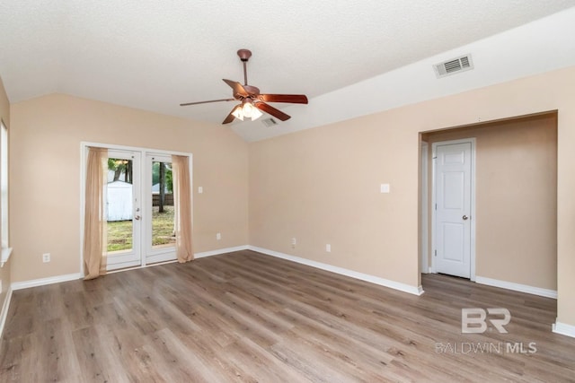 empty room with lofted ceiling, ceiling fan, a textured ceiling, light wood-type flooring, and french doors