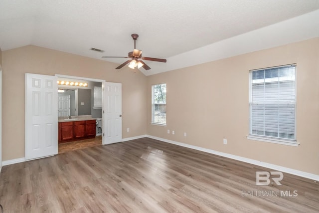 unfurnished bedroom with ensuite bathroom, vaulted ceiling, light hardwood / wood-style flooring, a textured ceiling, and ceiling fan