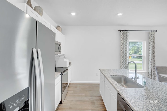 kitchen with sink, light wood-type flooring, appliances with stainless steel finishes, light stone counters, and white cabinetry