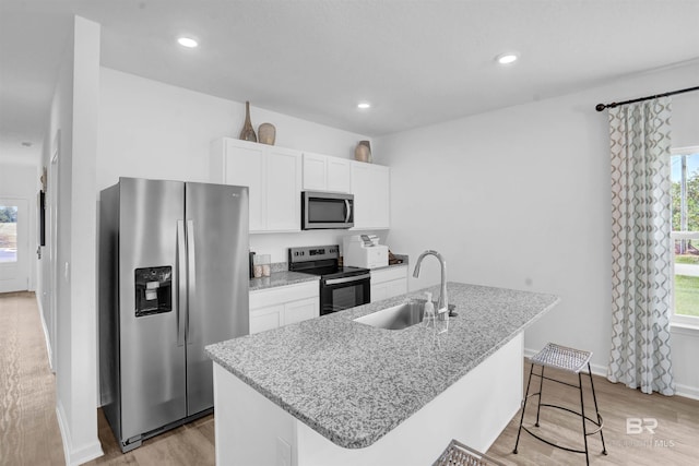 kitchen with light stone counters, stainless steel appliances, sink, a center island with sink, and white cabinets