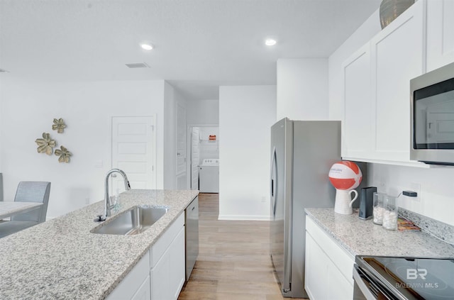 kitchen with white cabinets, light stone counters, washer / dryer, and sink