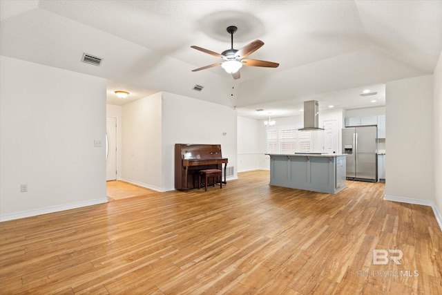 unfurnished living room featuring ceiling fan with notable chandelier and light wood-type flooring