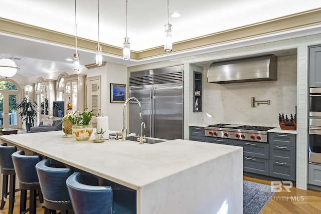 kitchen featuring light wood-style floors, light stone counters, gray cabinets, stainless steel appliances, and wall chimney range hood