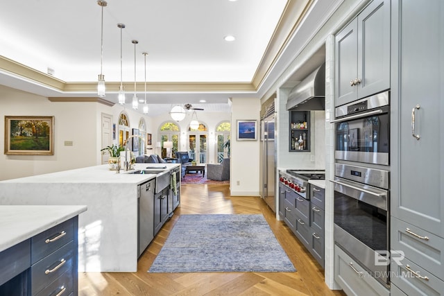 kitchen featuring light wood finished floors, wall chimney exhaust hood, appliances with stainless steel finishes, open floor plan, and a sink